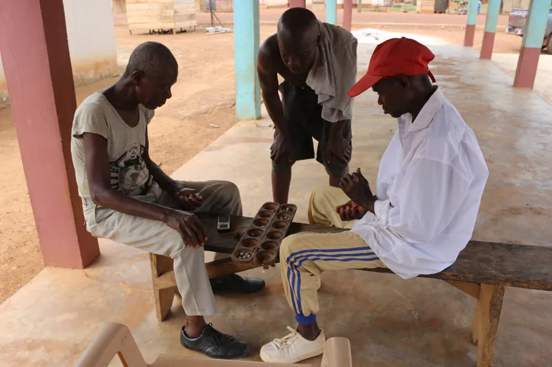 Hai người đàn ông chơi Oware tại Ghana, cùng một người đứng xem.